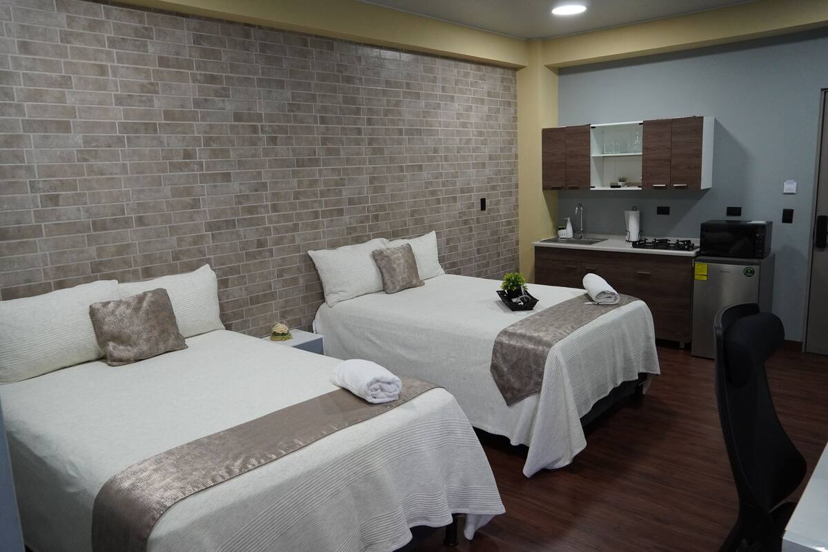 A hotel room with two beds, a small kitchenette, and a mirror above the counter.