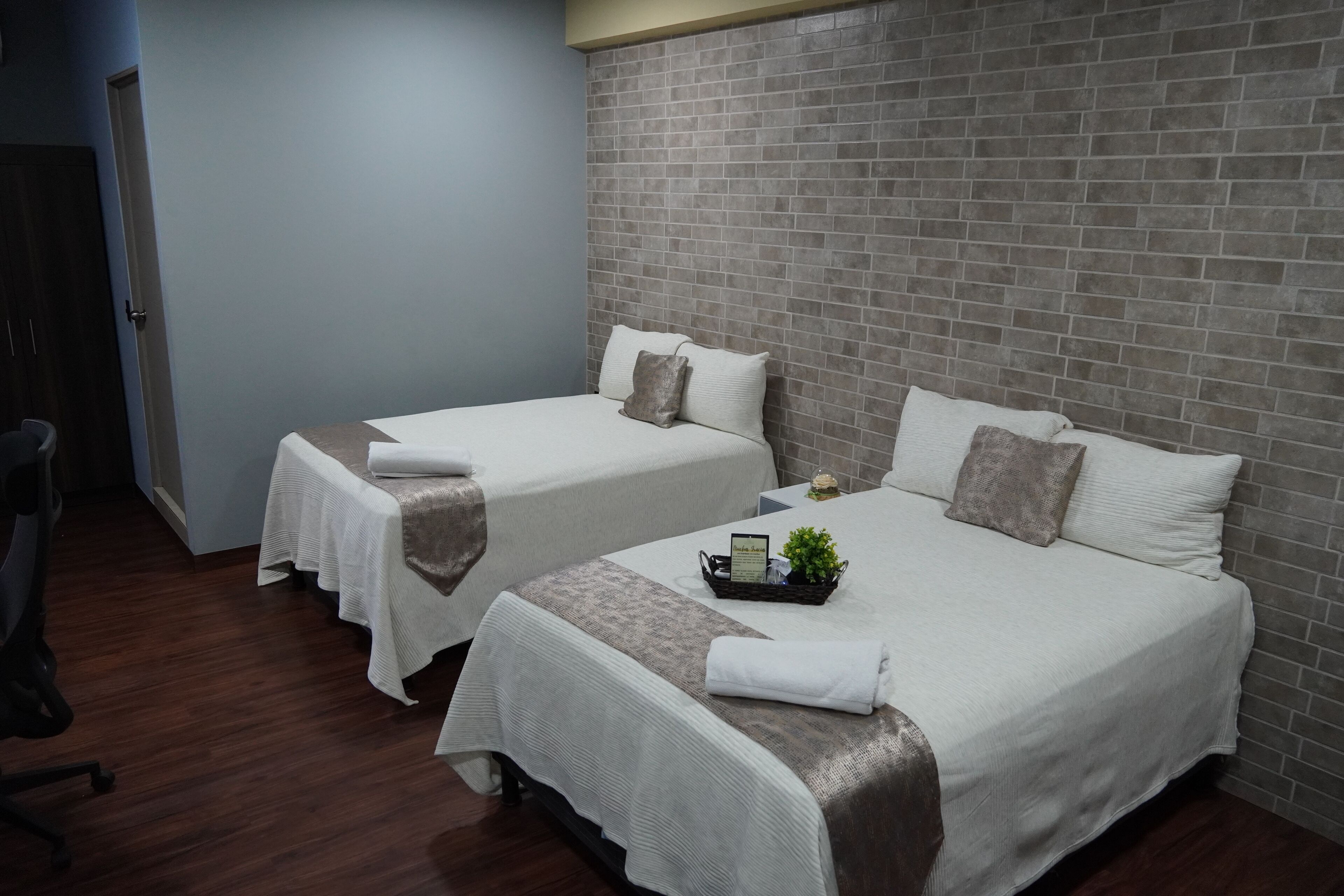 Ein Hotelzimmer mit zwei Betten, beide mit weißen Laken und einer braunen Tagesdecke. Dazwischen steht ein kleiner Tisch mit einer Pflanze und einer Speisekarte.