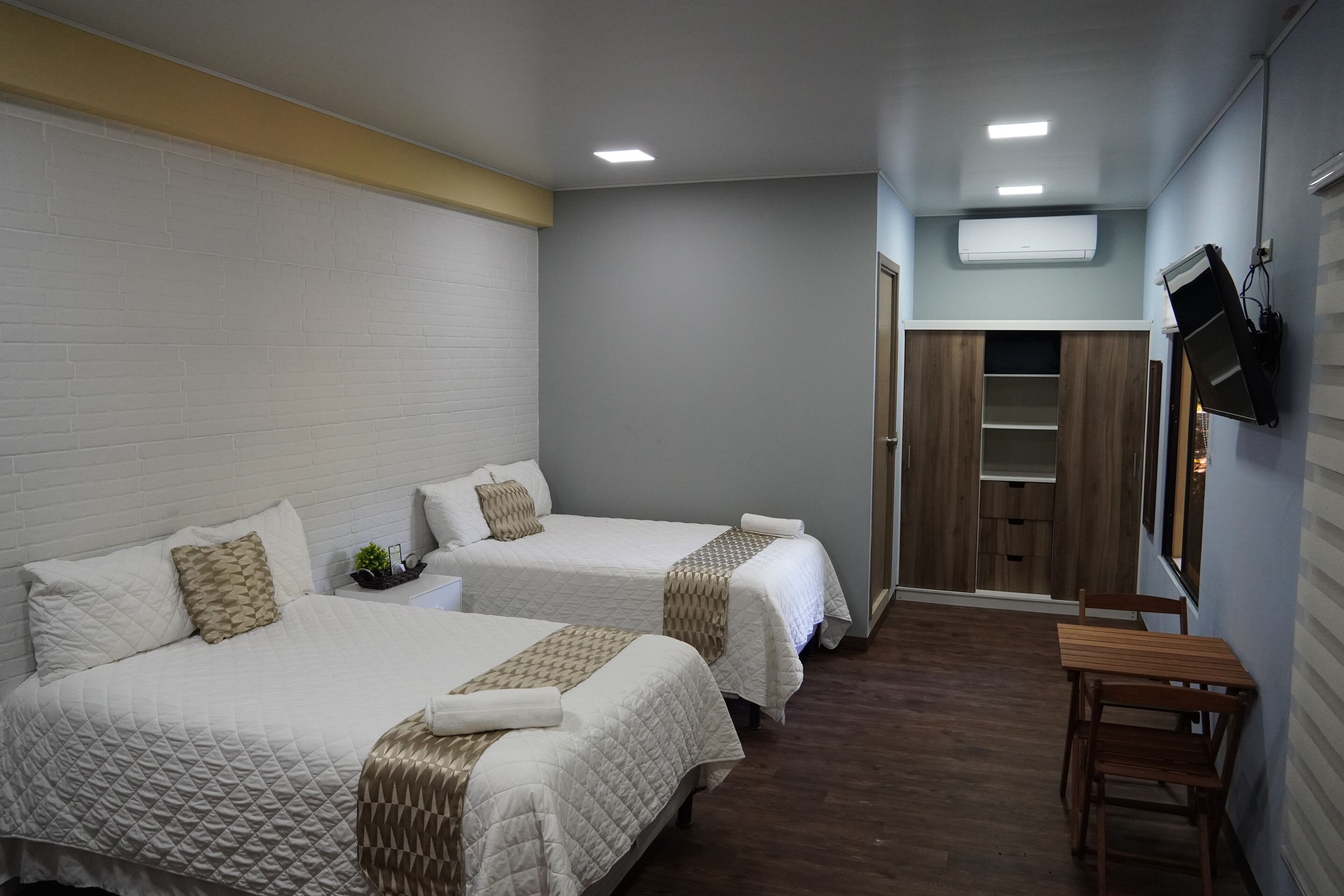 A hotel room with two beds, a wooden table, and a TV mounted on the wall.