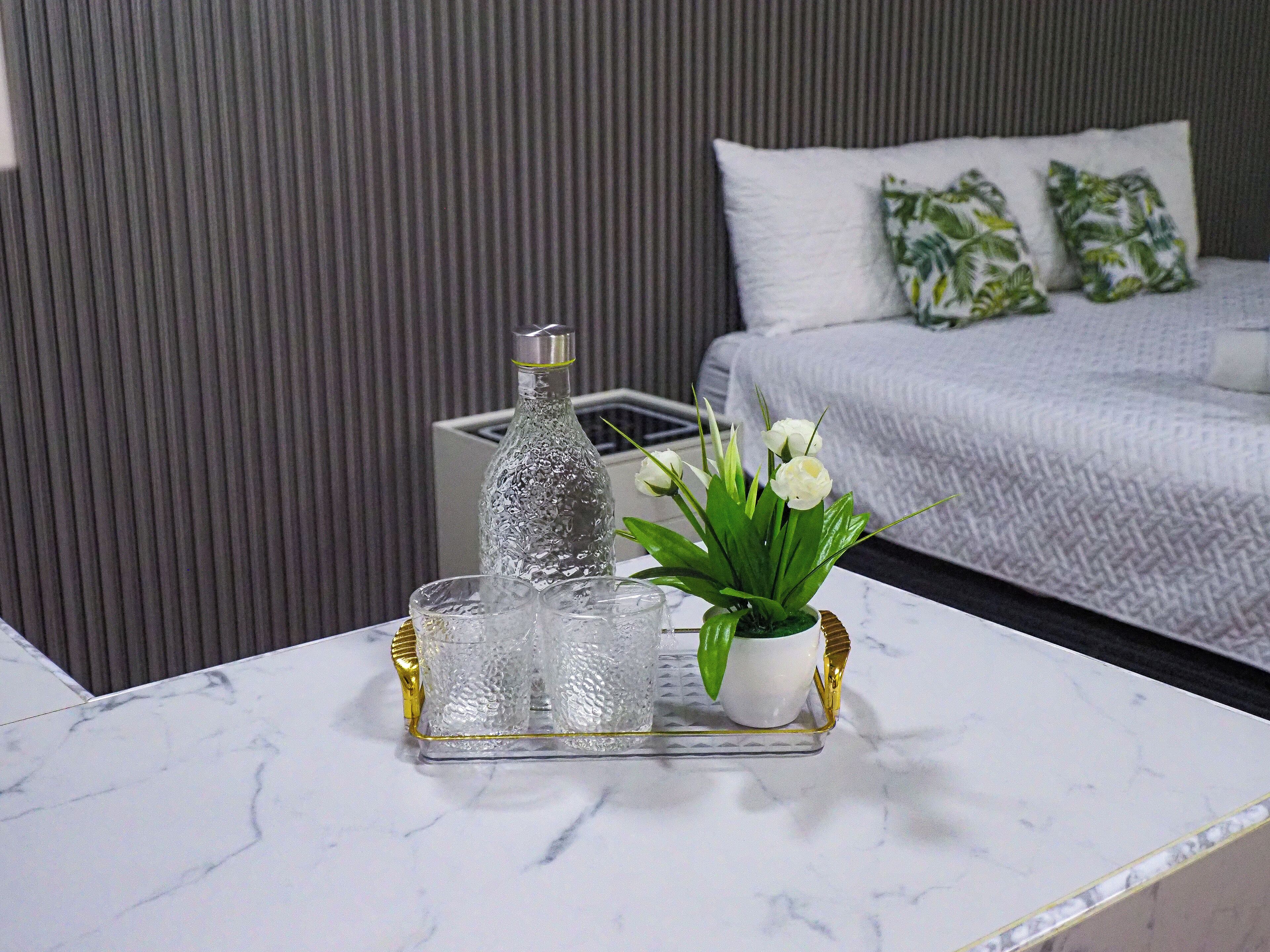 A marble table with a glass bottle, a glass carafe, and a potted plant with white flowers.