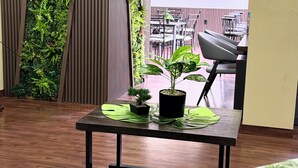 Una habitación con piso de madera, una pequeña mesa con plantas en macetas, una ventana con vista a mesas al aire libre y vegetación vertical.