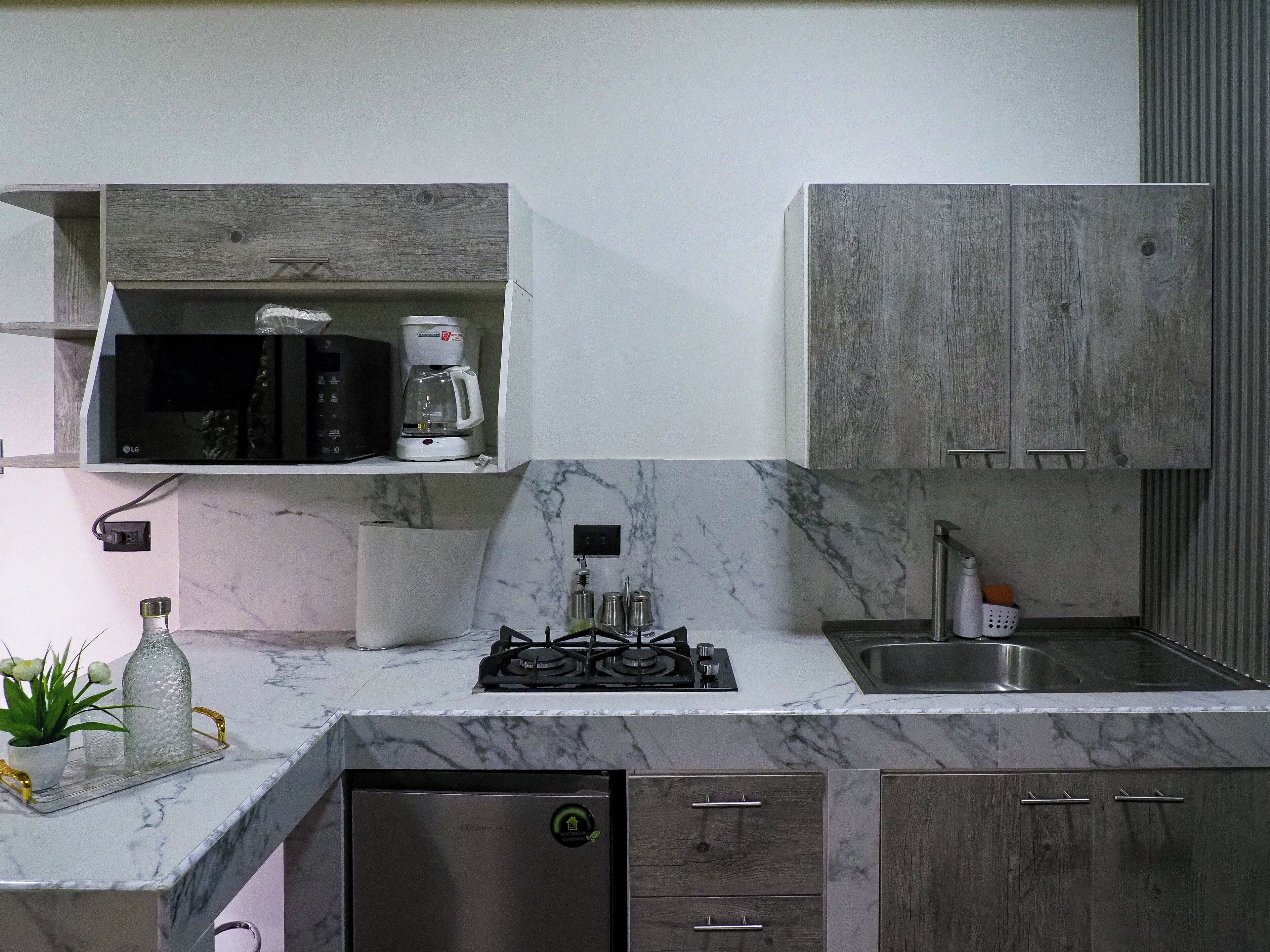 Een moderne keuken met een marmeren aanrecht, een ingebouwde magnetron, een koffiezetapparaat en een RVS spoelbak.