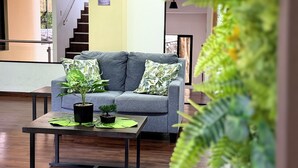 Una sala de estar moderna con un sofá gris, una mesa de centro con plantas y una escalera al fondo.