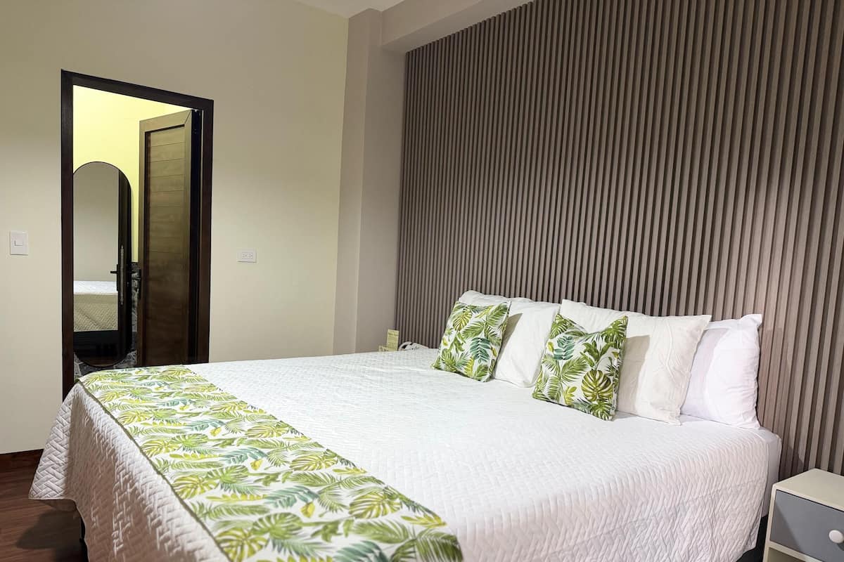 A hotel room with a bed, a nightstand, a mirror, and a door.