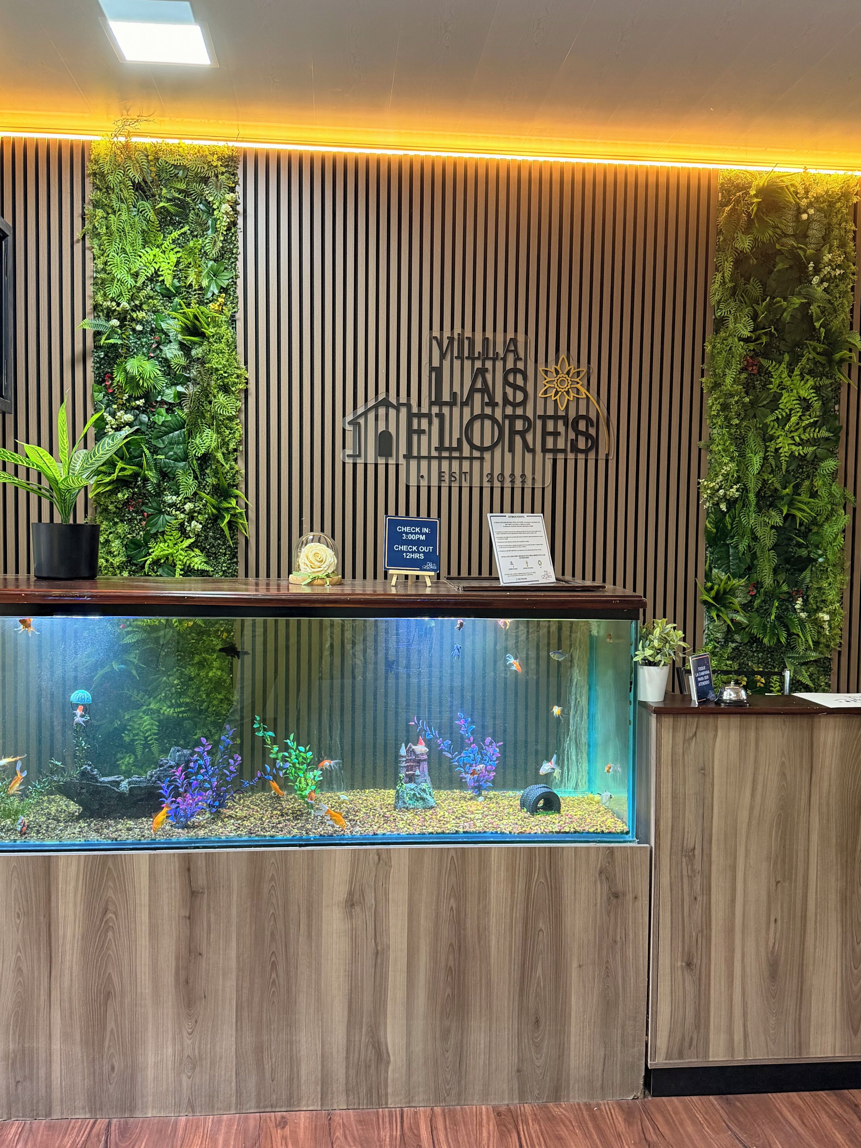 A reception desk with a vertical garden, a large aquarium, and a sign indicating check-in and check-out times.