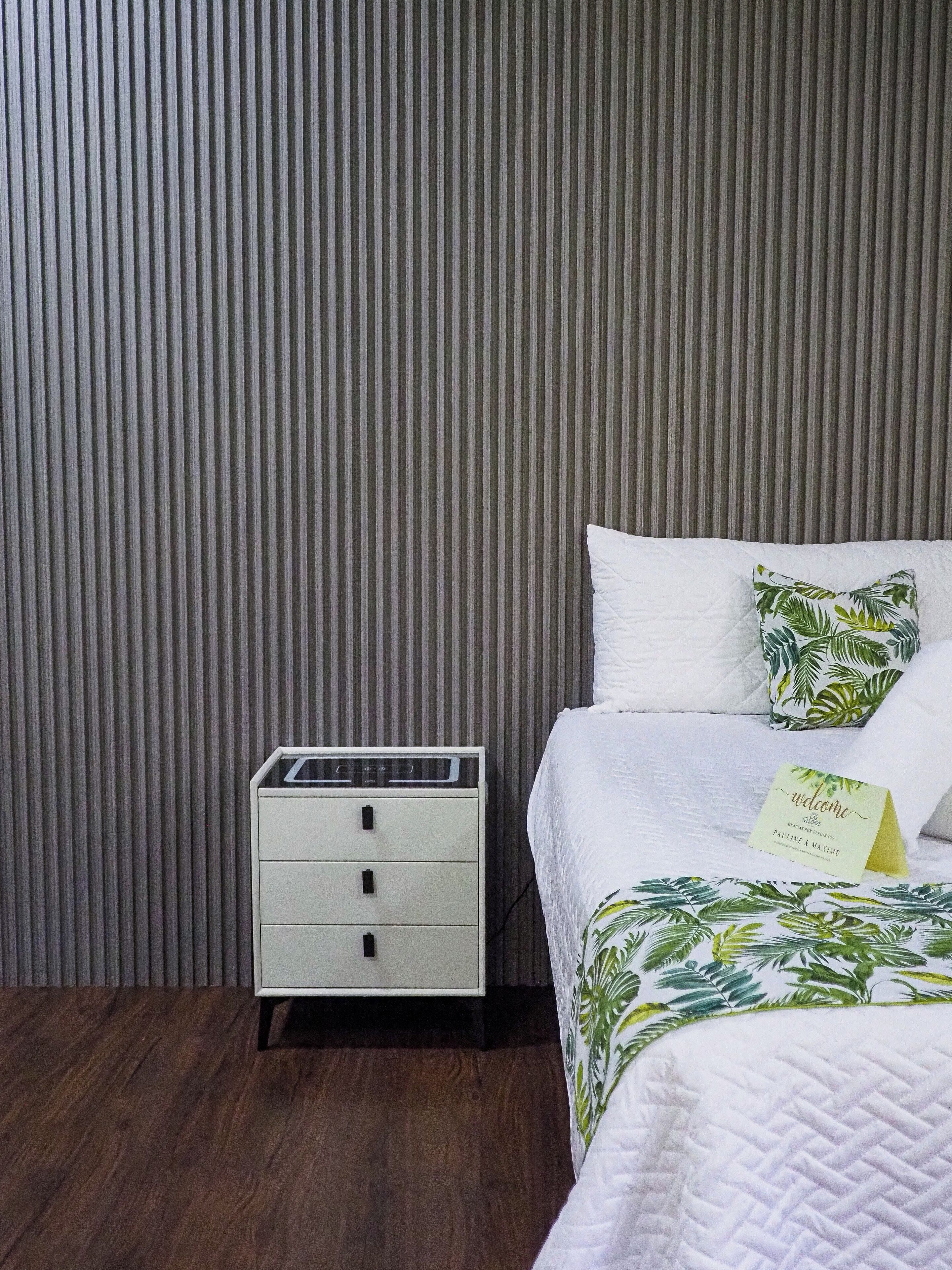 Une chambre d’hôtel avec un lit, une table de chevet et un mur orné de lignes verticales.