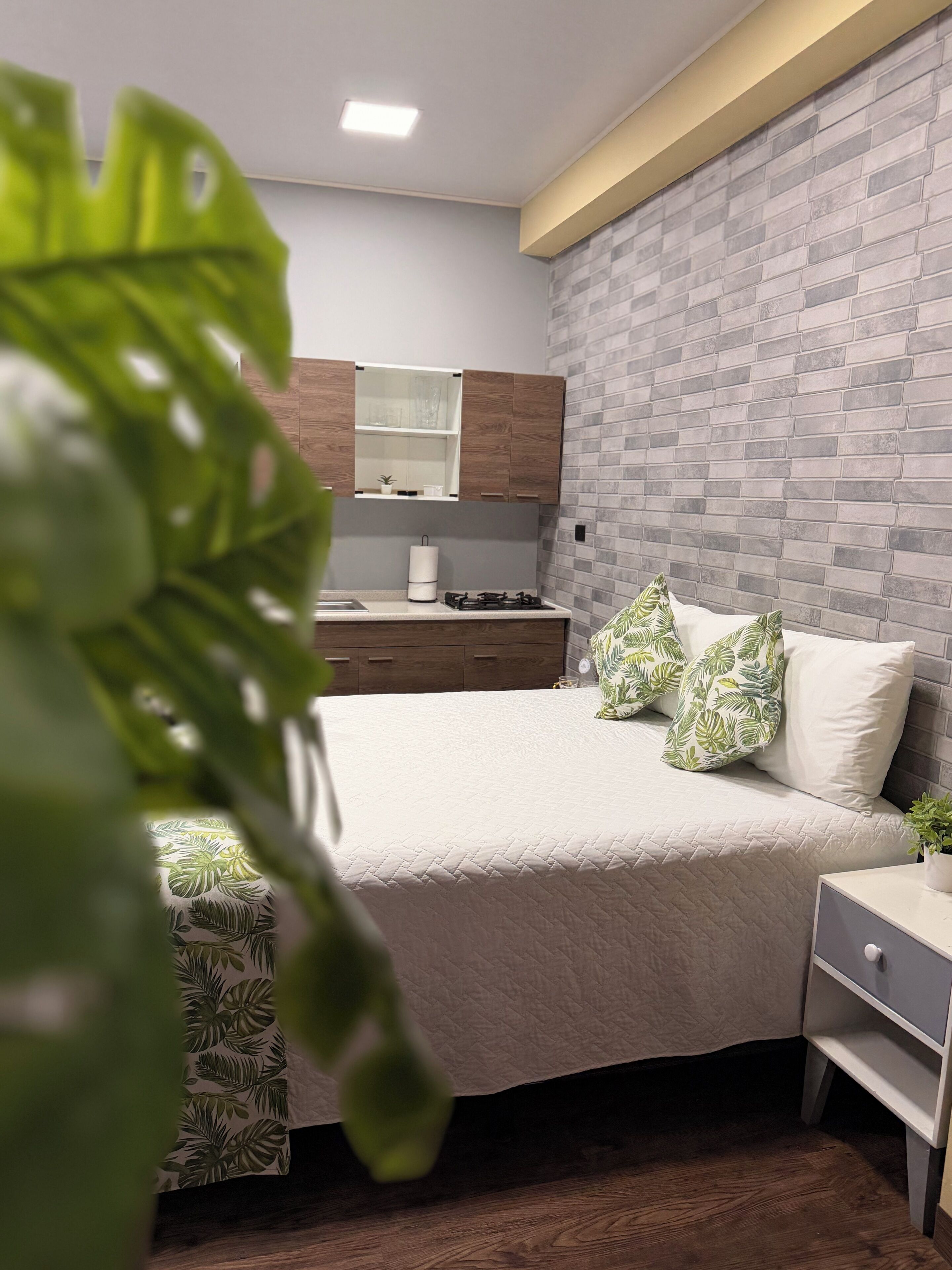 Een slaapkamer met een bed, nachtkastje en een klein keukenhoekje met een fornuis.