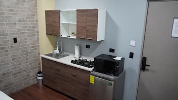 Une cuisine de taille réduite, équipée d’une cuisinière, d’un four à micro-ondes, d’un évier et de meubles de rangement en bois.
