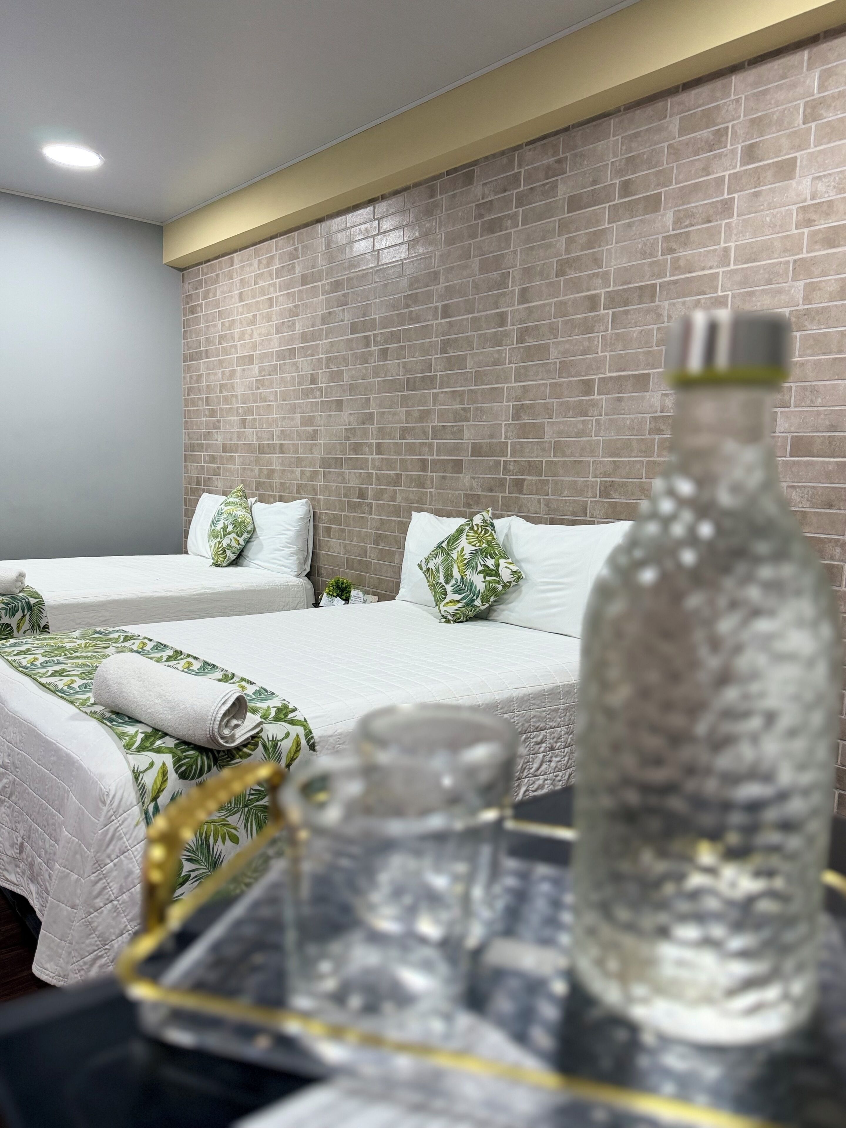 Ein Hotelzimmer mit zwei Betten, einer Wand mit Backsteinmusterung und einem kleinen Tisch mit Flasche und Glas.