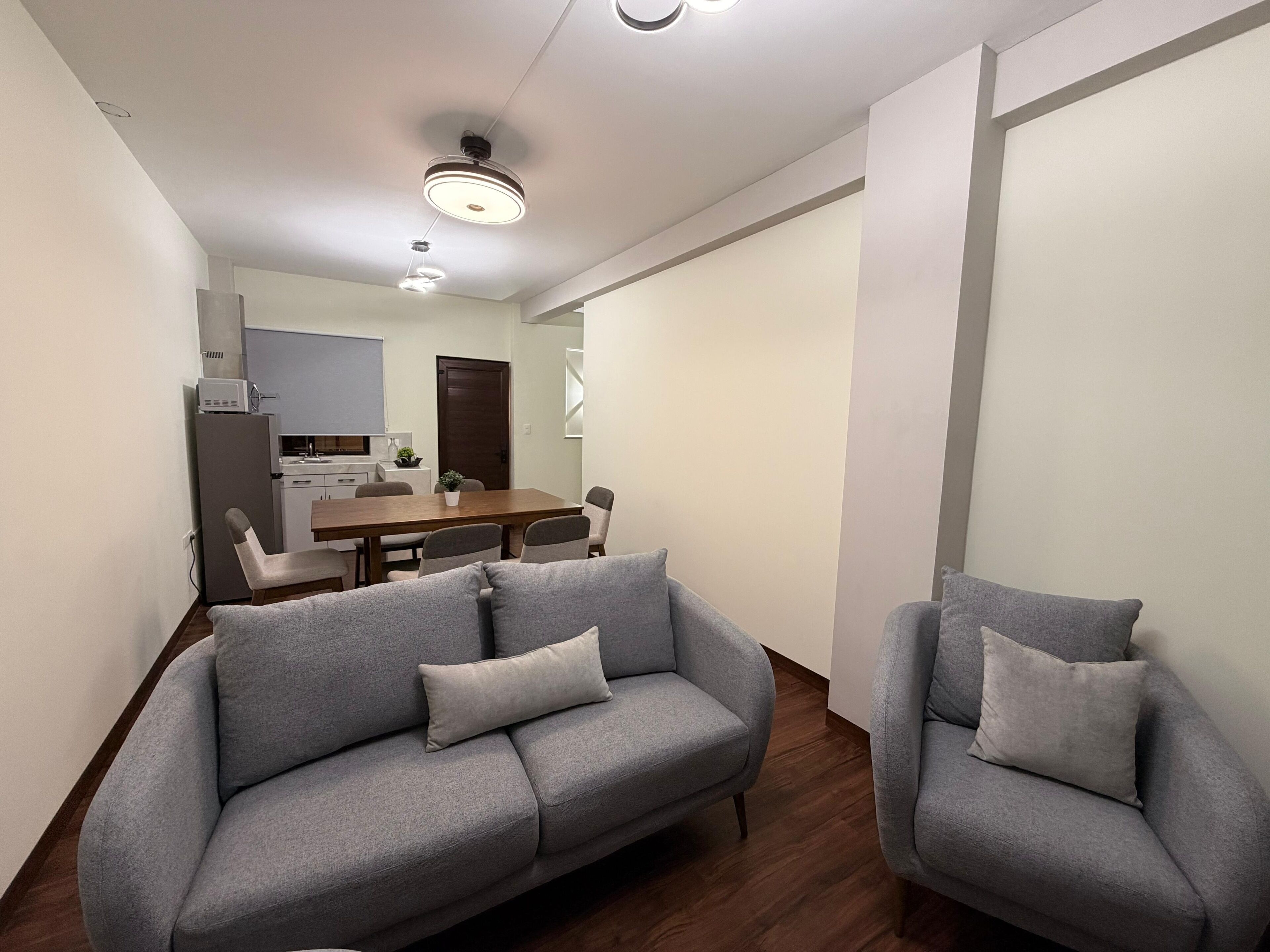 Una sala de estar moderna con un sofá gris, una mesa de comedor y una cocina al fondo.