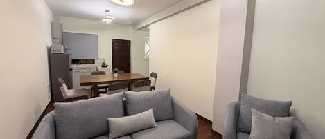 Una sala de estar moderna con un sofá gris, una mesa de comedor y una cocina al fondo.