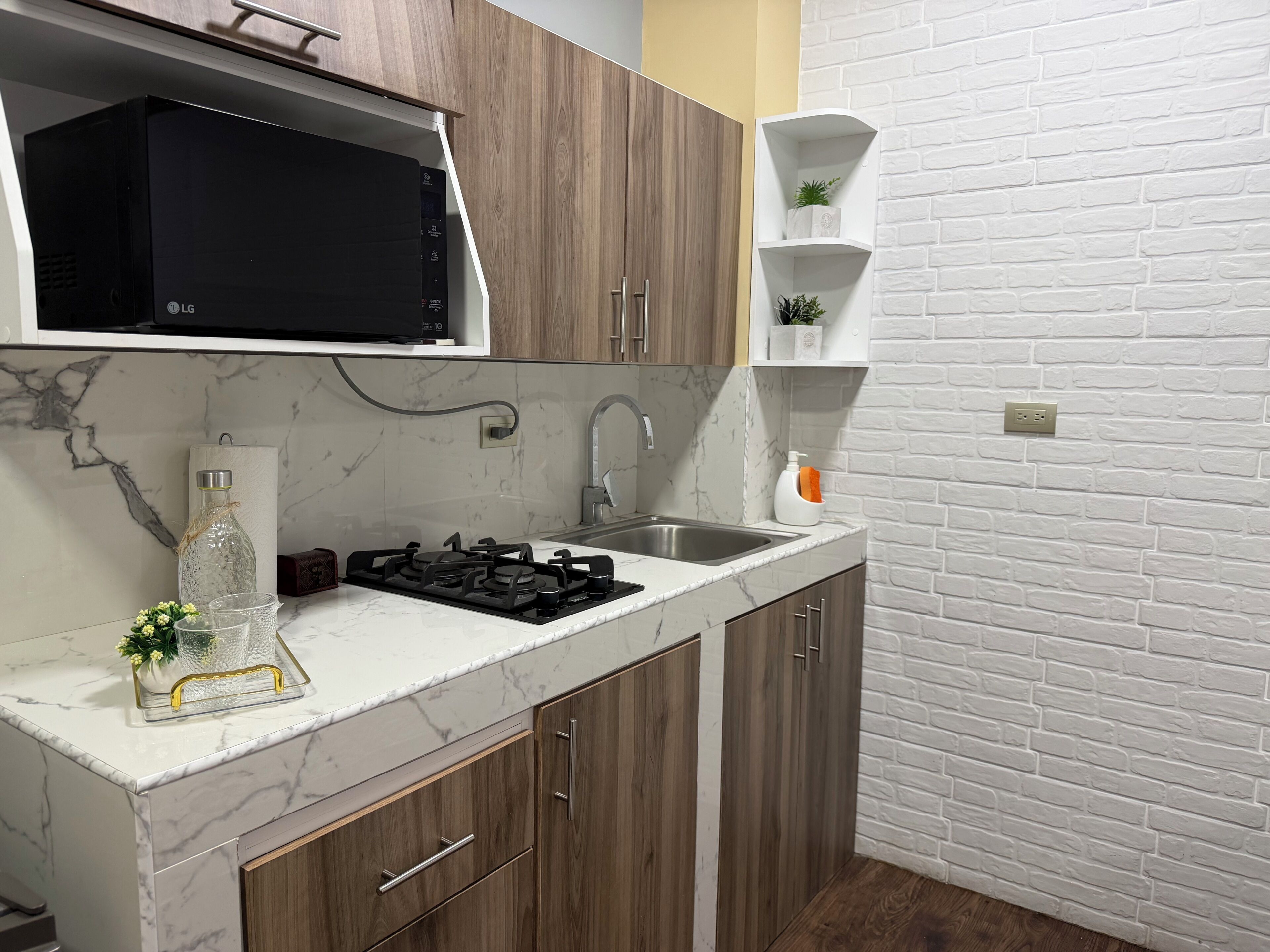A kitchen with a gas stove, a microwave, wooden cabinets, a marble countertop, and a white brick wall.