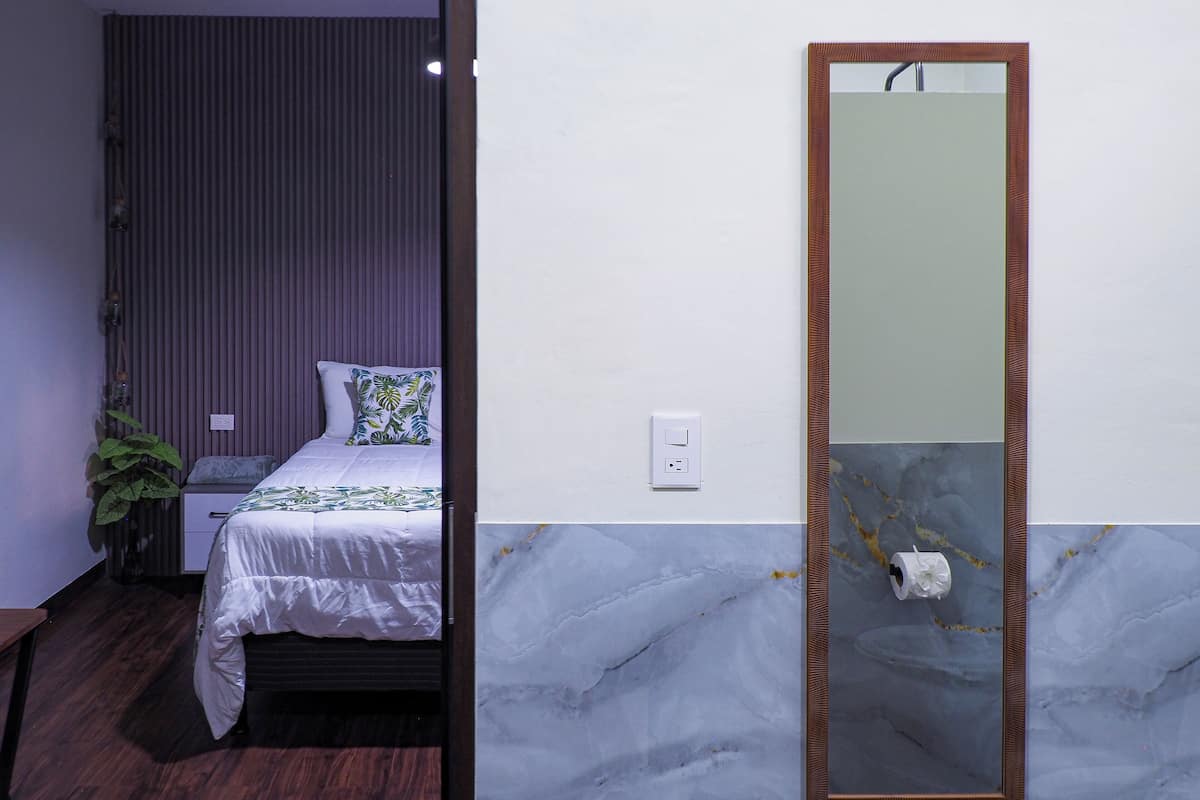 A bedroom with a bed, a nightstand, a potted plant, a wall-mounted mirror, and a marble accent wall.
