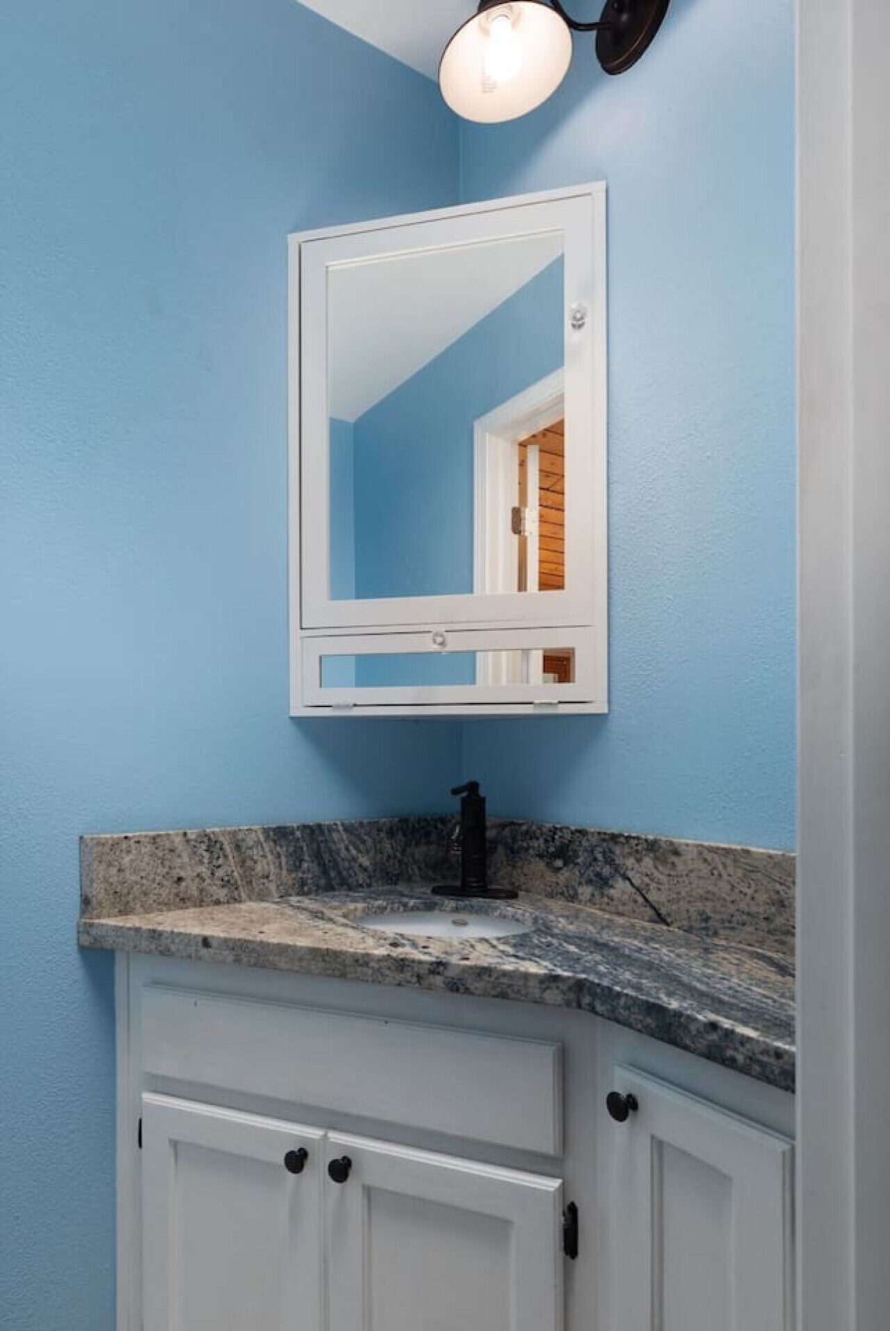 A bathroom with a blue wall, a white vanity with a granite countertop, a black faucet, and a mirror above the vanity.