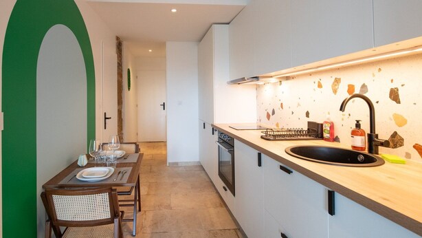 A modern kitchen with a wooden countertop, a black sink, and a backsplash with stone-like tiles. - Valencio - Superb cosy apartment (Lyon)
