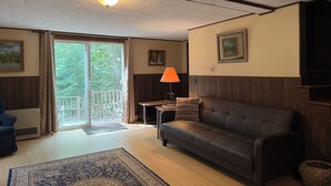 Una sala de estar con un sofá de cuero, un tapete estampado, una mesa con lámpara, un cuadro en la pared y un ventanal corredero que da a un balcón.