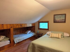 Quarto com uma cama de solteiro, uma cama individual, uma pequena mesa, uma janela e um quadro na parede.