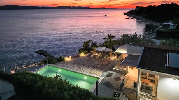 Una casa moderna amb piscina, mobiliari exterior i vistes al mar al capvespre.