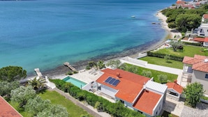 Zona residencial a la costa, amb cases, mar blau clar i piscina.