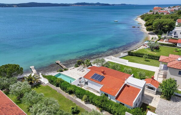 Un quartier résidentiel en bord de mer, avec des maisons, une mer d’un bleu limpide et une piscine.