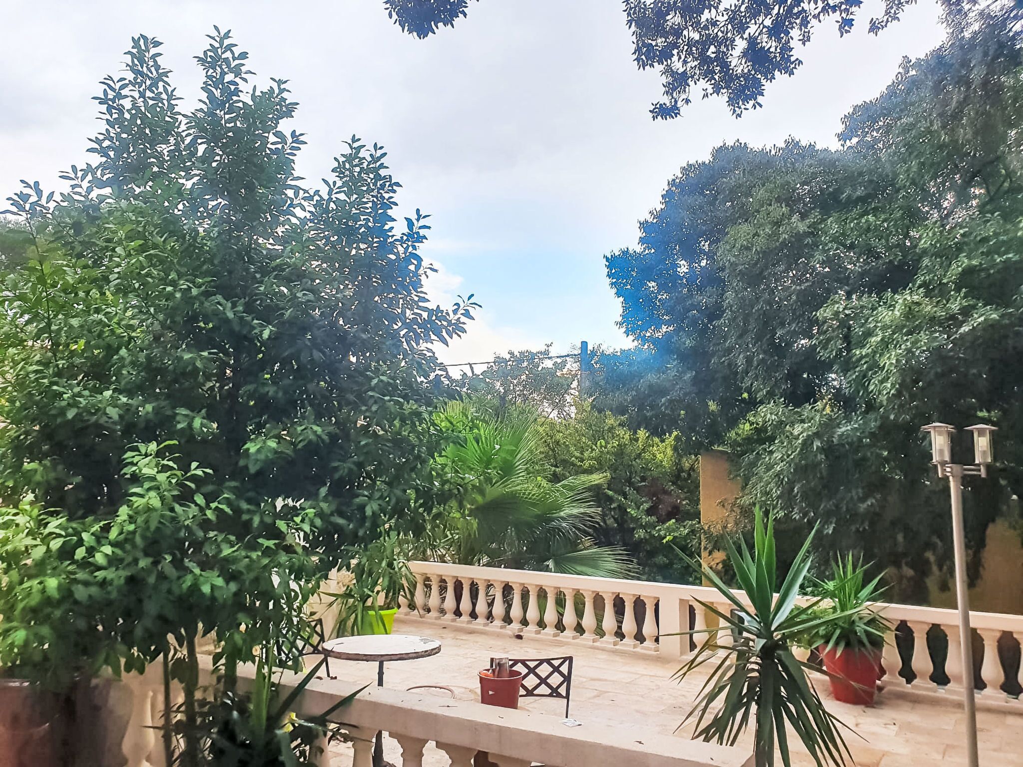 A courtyard with a table and chairs, surrounded by lush greenery and a decorative railing.