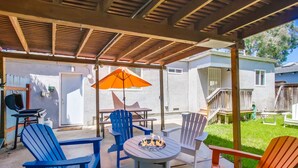 En udendørs patio med bålsted, blå og røde Adirondack-stole og en træpergola.