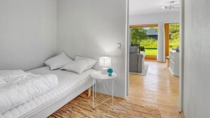 Ein modernes Schlafzimmer mit Bett, Nachttisch und Blick auf einen Garten durch eine offene Tür.