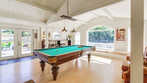 Amplia habitación con mesa de billar, piso de madera y un ventanal con vistas al exterior.