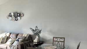 Un coin repas avec une table en verre, des chaises en bois et un canapé gris agrémenté de coussins.