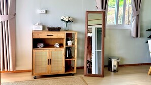 Une pièce avec un meuble en bois, un miroir, une fenêtre avec des rideaux et une petite poubelle.
