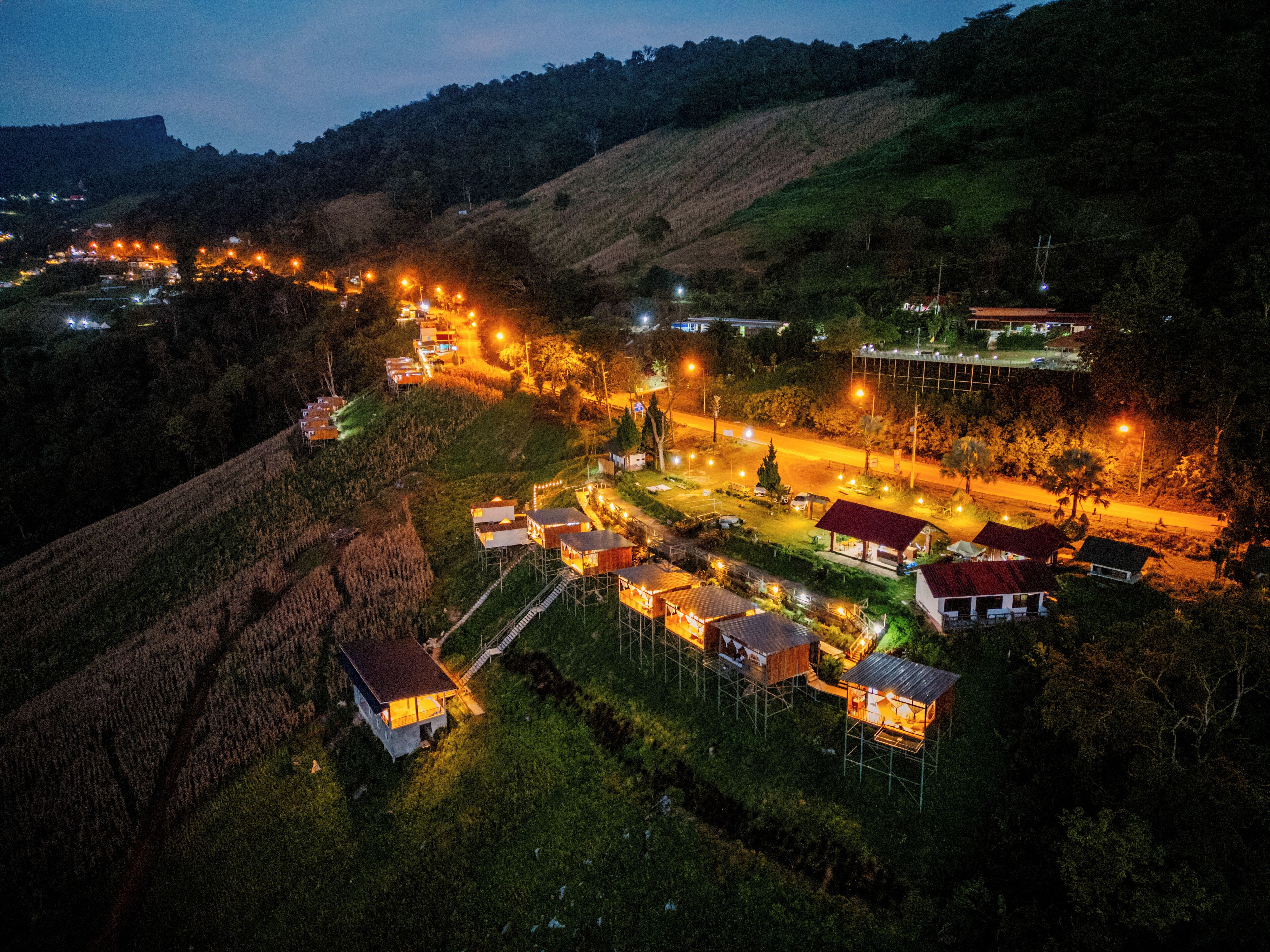 Un pueblo en la ladera de una colina, iluminado de noche, con una carretera.