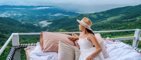 A person sitting on a bed with a view of a mountainous landscape.