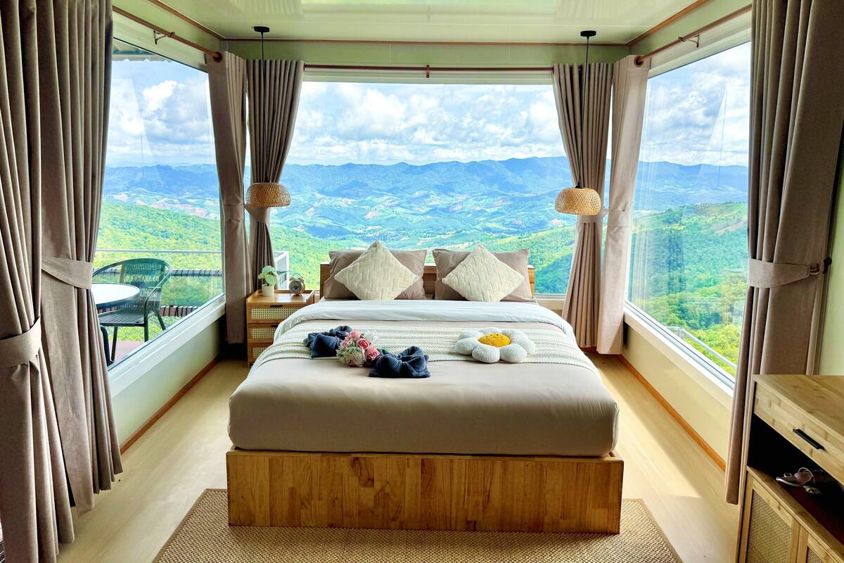 Une chambre dotée d’un grand lit, d’une table de chevet, d’une chaise et offrant une vue sur un paysage montagneux grâce à de grandes fenêtres.