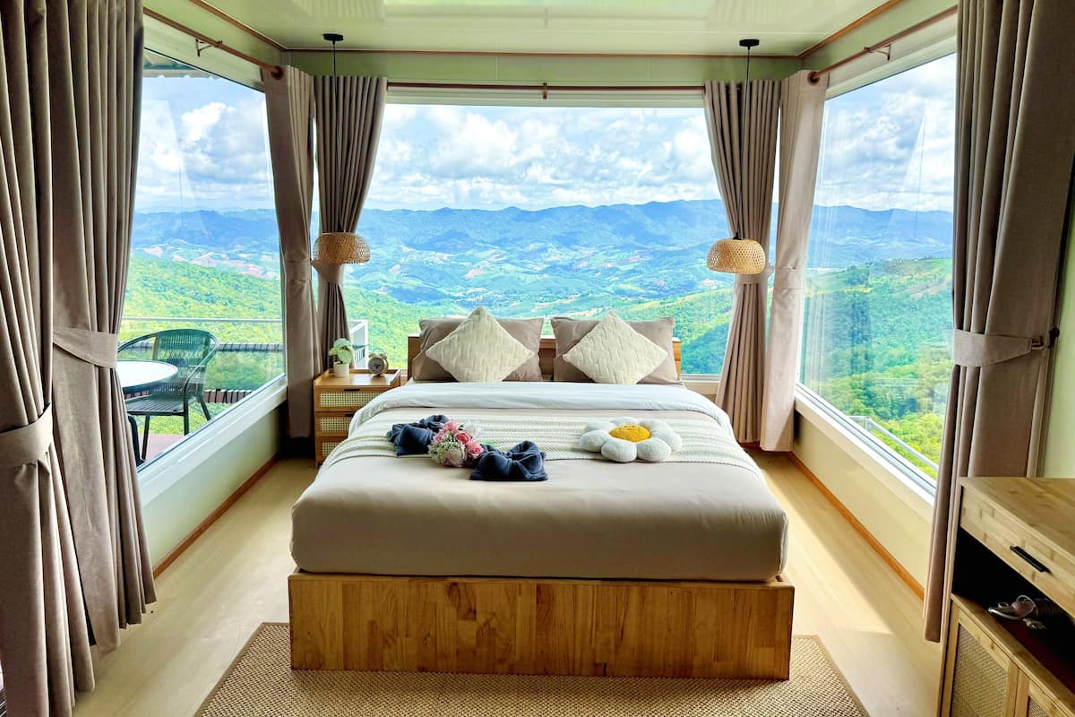 Une chambre dotée d’un grand lit, d’une table de chevet, d’une chaise et offrant une vue sur un paysage montagneux grâce à de grandes fenêtres.