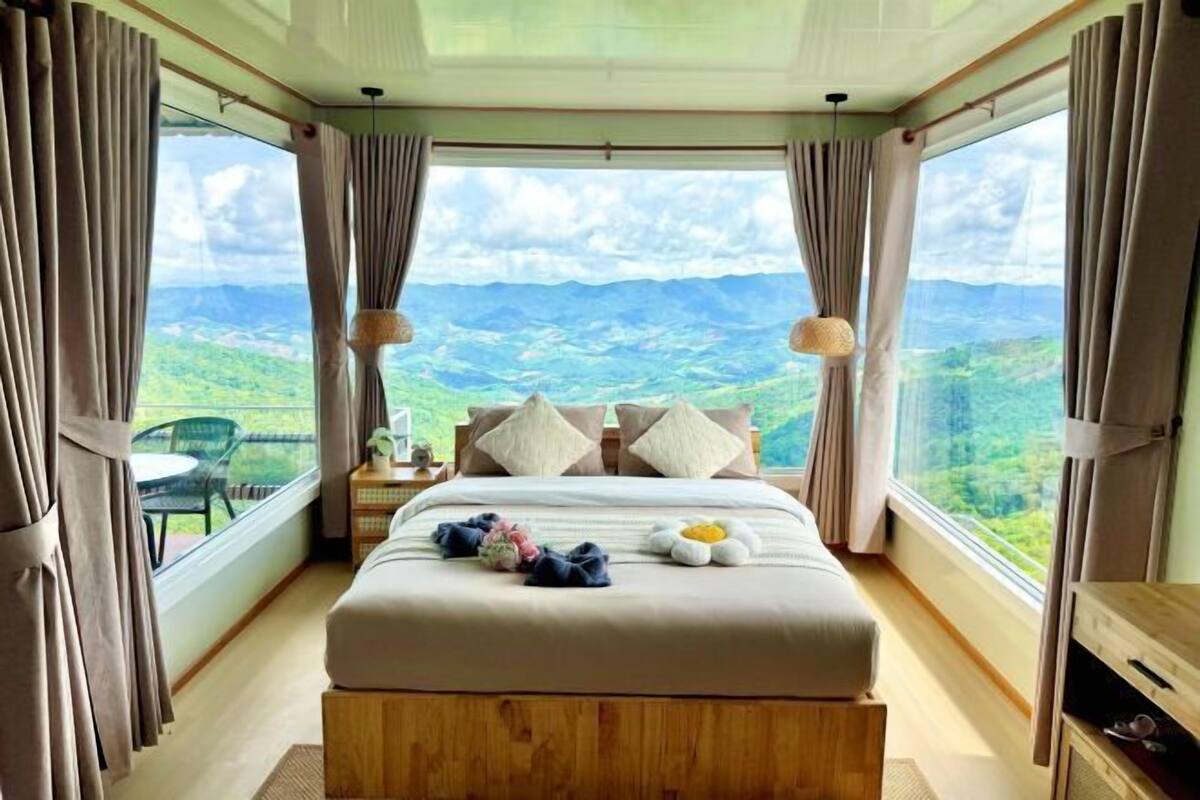 Une chambre à coucher avec un grand lit, des rideaux, une table de chevet et une vue sur un paysage montagneux.