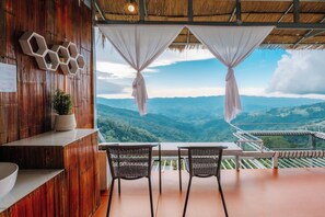 A terrace with two wicker chairs and a table, overlooking a mountainous landscape. - Long Hak Khao Camping Phu Chi Fa (Thoeng)