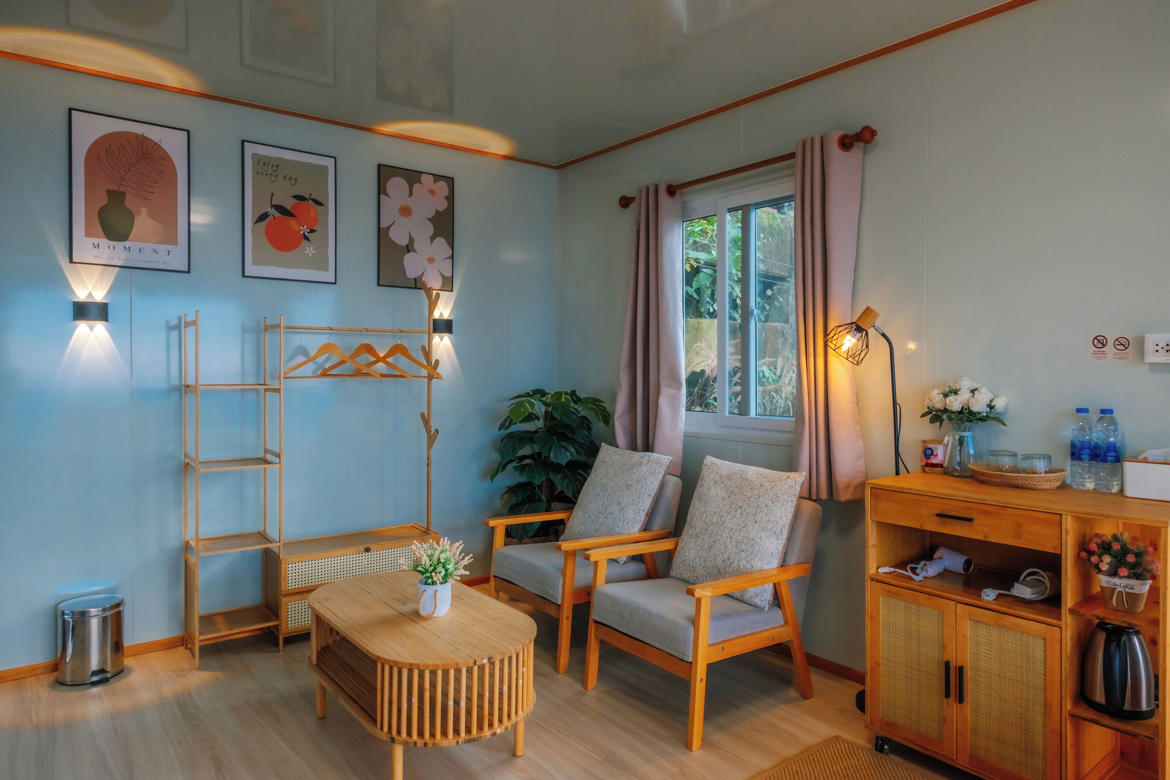 A cozy room with a wooden floor, a round wooden table, two cushioned chairs, a small cabinet, and wall-mounted light fixtures.