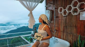 A woman sitting in a large bathtub with a view of mountains in the background.