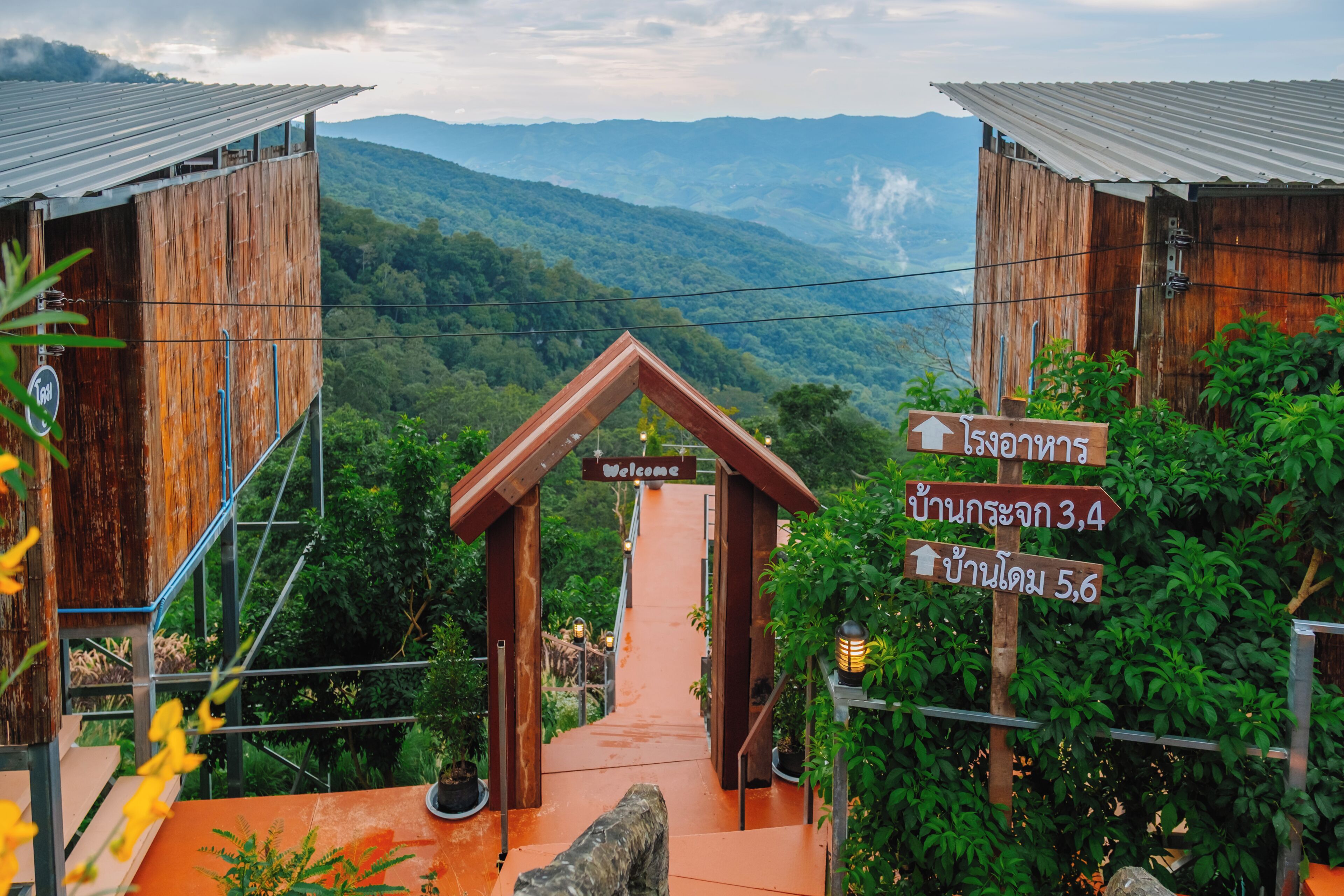 Una estructura de madera con un cartel que dice 'Welcome', rodeada de exuberante vegetación y un paisaje montañoso.