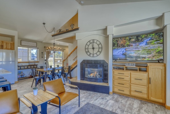 A spacious living area with a fireplace, a large TV, wooden furniture, and a staircase leading to an upper level.