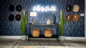 A room with a dark blue patterned wall, a neon sign, a desk with baskets, and cacti. - Sport Court | Private Heated Pool | Mini Golf & More (Glendale)