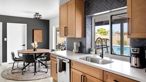 A modern kitchen with wooden cabinets, a white countertop, a built-in sink, and a view of a swimming pool. - Sport Court | Private Heated Pool | Mini Golf & More (Glendale)
