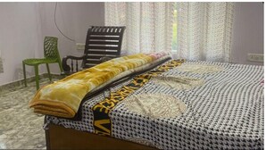 Een slaapkamer met een bed, een groene stoel, een zwarte stoel en een raam met gordijnen.