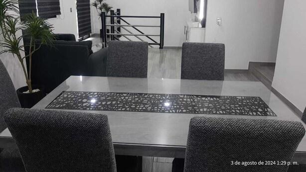 Een moderne eetruimte met een tafel met glazen blad, gestoffeerde grijze stoelen en een trap naar een hoger niveau.