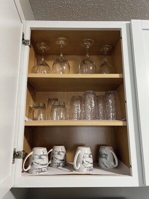 Un mueble con copas de vino en el estante superior y tazas de café en el inferior.