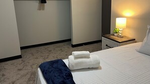 Ein Hotelzimmer mit Bett, Nachttisch mit Lampe, Handtuch und Kleiderhaken.