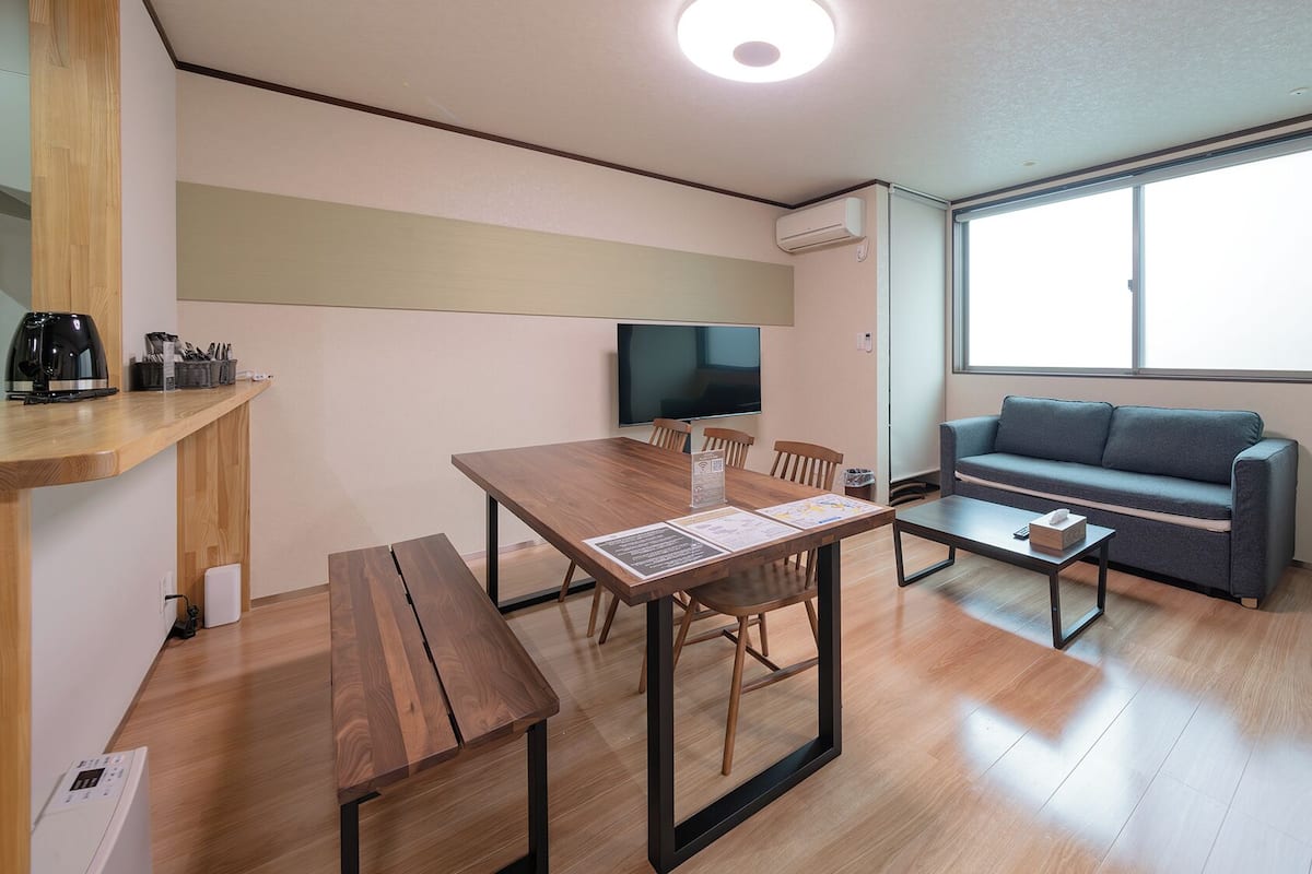 A modern living room with a wooden dining table, a sofa, and a large window.
