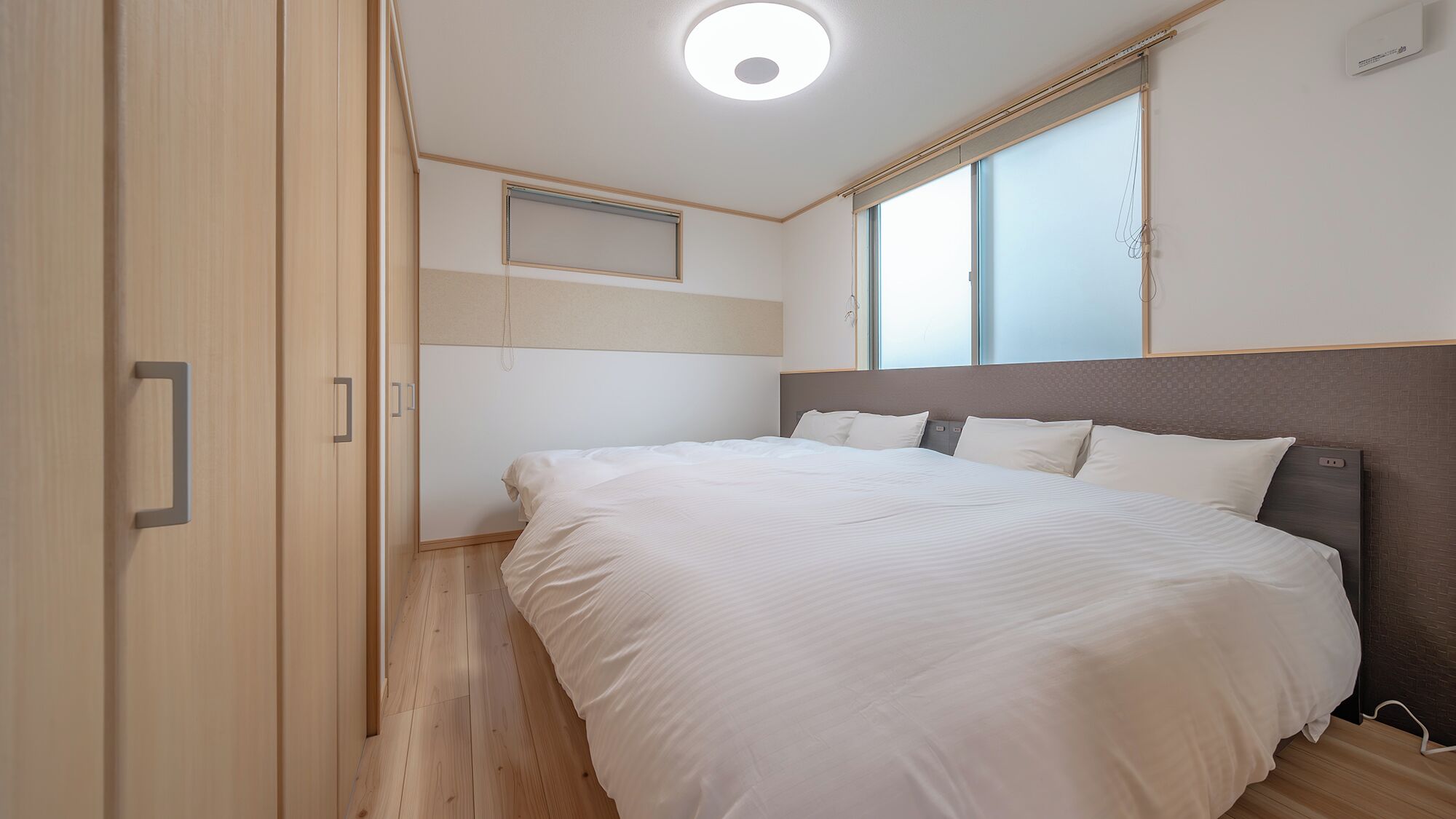 Ein Schlafzimmer mit einem großen Bett, Holzboden, einer Deckenleuchte und einem Fenster.