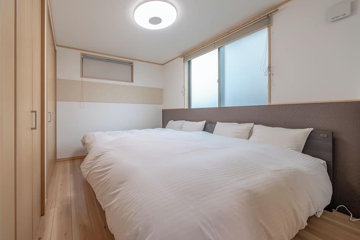 A bedroom with a large bed, wooden flooring, a ceiling light, and a window.