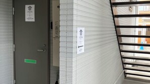 A narrow corridor with a grey door, a white brick wall, and a metal staircase. - Takayama Stay Karatachi DX-B (Takayama)